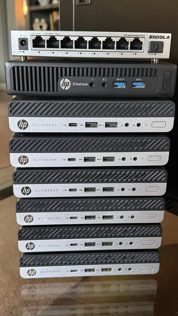 A stack of seven HP EliteDesk mini PCs with an eight-port network switch on top