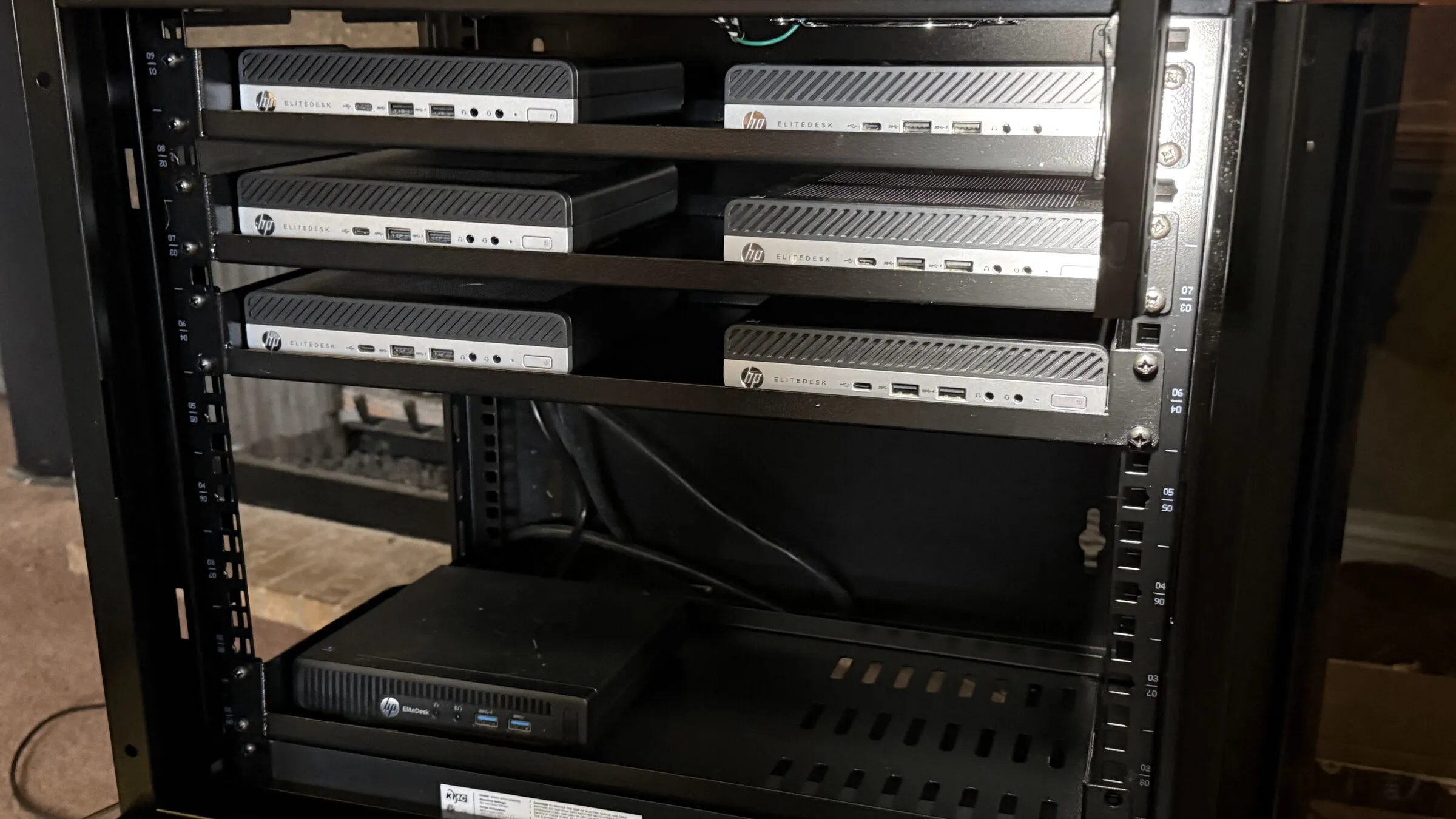 Six HP EliteDesk mini PCs on three shelves in an open wall cabinet, with an older black EliteDesk on the bottom shelf