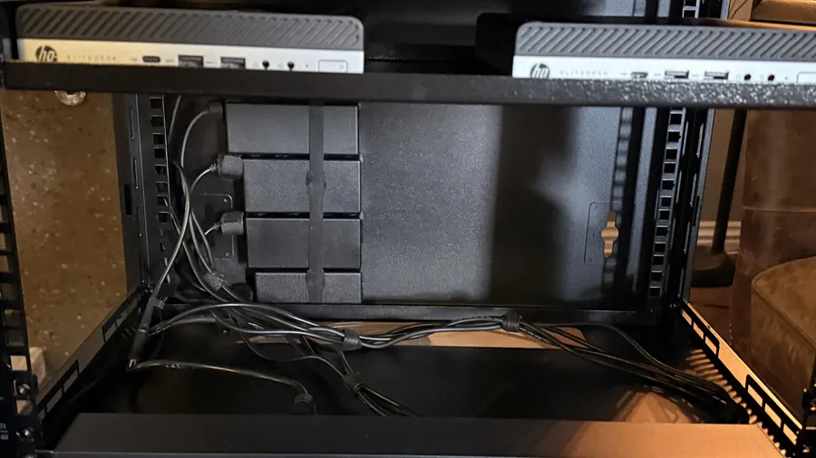 Power bricks strapped to the back wall of a server cabinet, with cables routed beneath two mini PCs